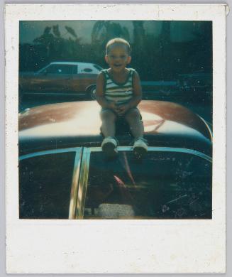 [Boy on car roof smiling, wearing striped tank top]