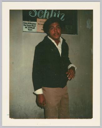 [Man in black sweater standing in front of sign, "Schlitz"]