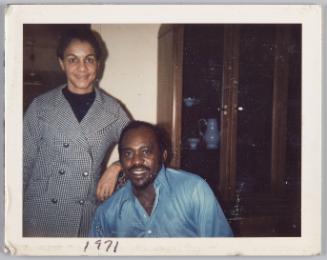 1971 [Woman in houndstooth jecket standing beside seated man]
