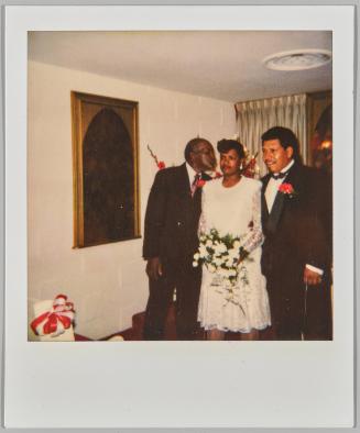 [Woman in white dress holding bouquet of white flowers with two men in suits and red  boutonnieres]