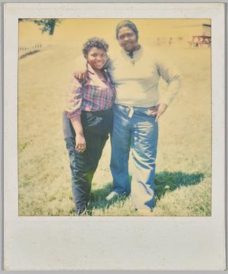 [Man with arm around woman in plaid shirt and standing on lawn]