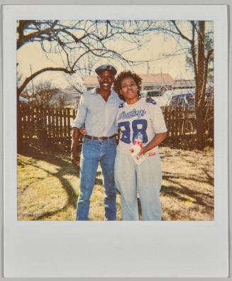 [Man and woman standing together outside in fenced area, woman wearing shirt with numberr "88" printed on the front]
