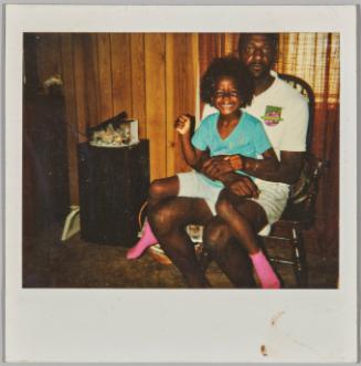 [Young girl wearing pink socks, smiling and sitting on man's lap in chair]
