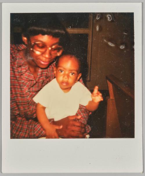 [Woman wearing glasses and plaid outfit holding baby, baby has one hand raised up]
