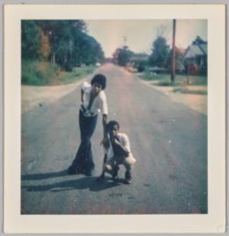 [Two men posing together in the centre of the street, man on right is crouching and man on left is leaning with legs crossed]
