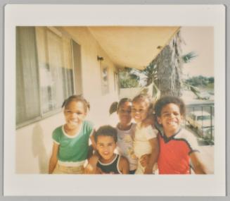 [Five children posing and smiling in a group on balcony with trees in background]
