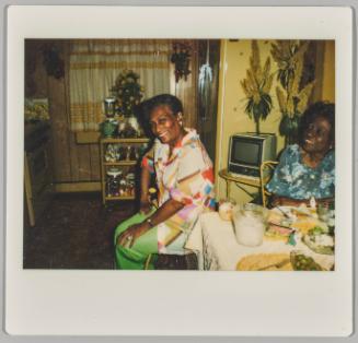 [Two women sitting at dining table smilign, woman on left has hands on thighs and is sitting sideways]
