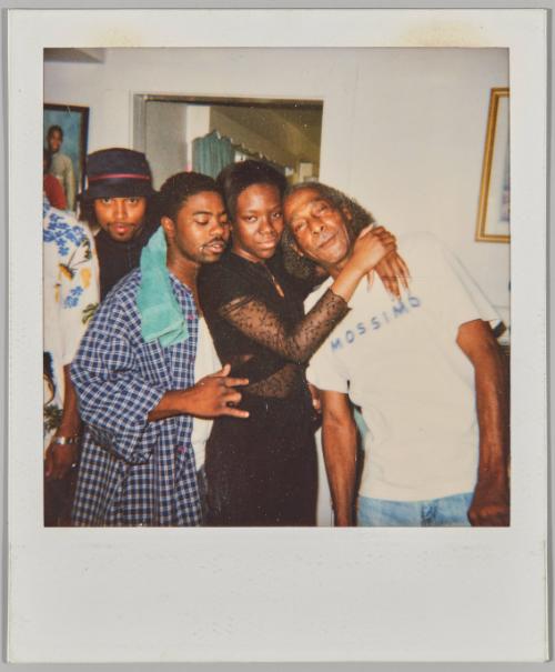 [Three men and a woman posing as a group in home, man on right wearing a graphic t-shirt stating ‘MOSSIMO’]
