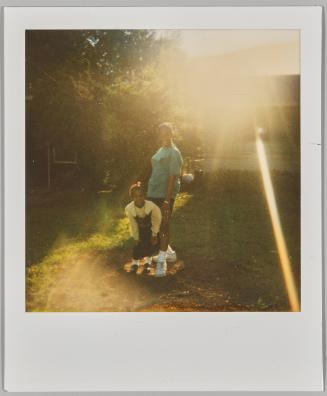 [Woman and little girl outside in yard with sunlight causing lens flare on upper right corner]
