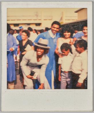 [Blurry group photo, young man in hat leans leans forward]
