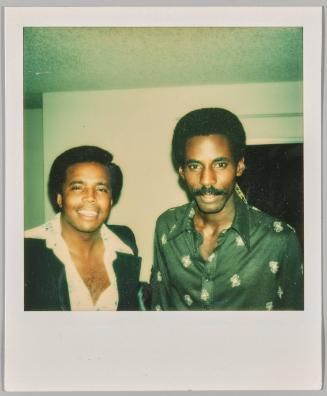 [Man with moustache and navy button-up standing next you man in white shirt partially unbuttoned]
