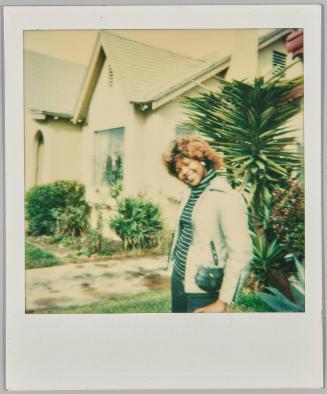 [Woman in striped turtleneck smiling in front of house with tropical plants in background]
