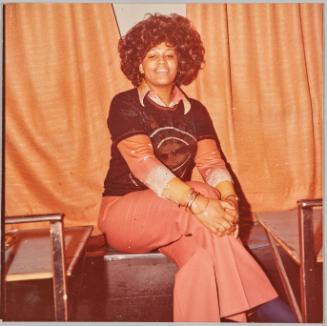 [Woman with thick, curly hair sitting crosslegged on metal bench]
