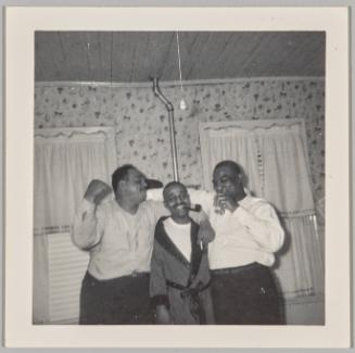 [Three cheery men posing, man in the middle holds pipe in his mouth]
