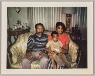 [Man and woman sitting on couch, little boy sitting on woman's lap holding a toy car]
