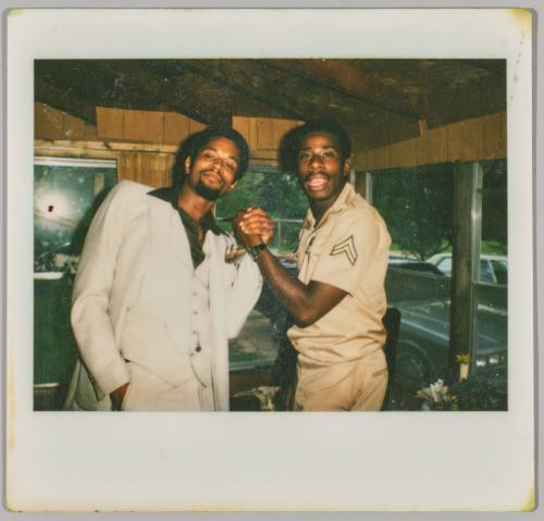 [Man in suit clasping hands with man in military uniform] 
