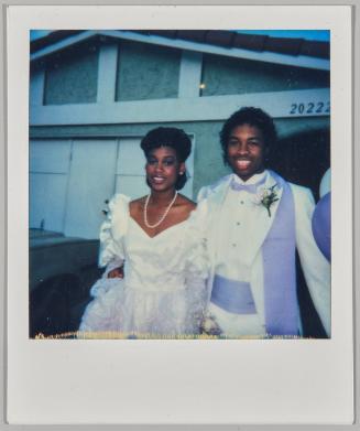 [Woman in white dress posing with man in white and purple tuxedo]
