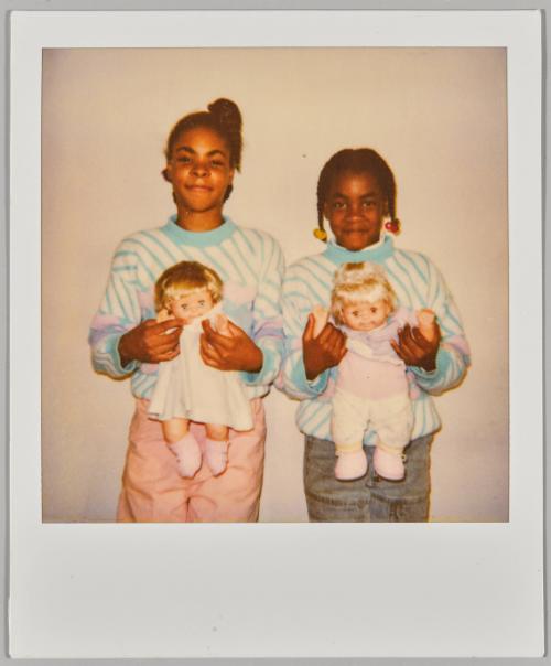 [Two girls posing in matching sweaters holding baby dolls]
