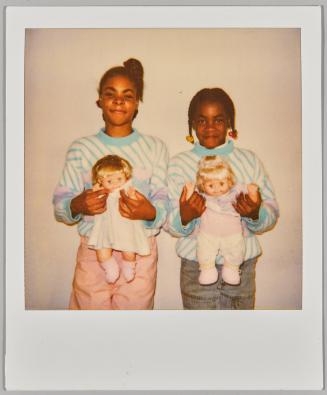 [Two girls posing in matching sweaters holding baby dolls]
