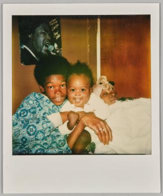 [Woman with headwrap laying under blanket with two boys]
