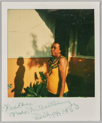 July 4, 1980 [Woman standing outside house in sun with plants]
