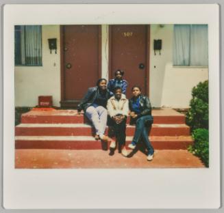 [Four young women sitting on steps in front of two doors outside]
