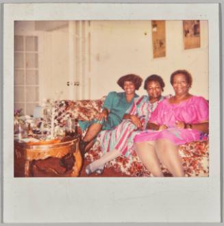 [Three women on floral couch with tree scultpure on table]
