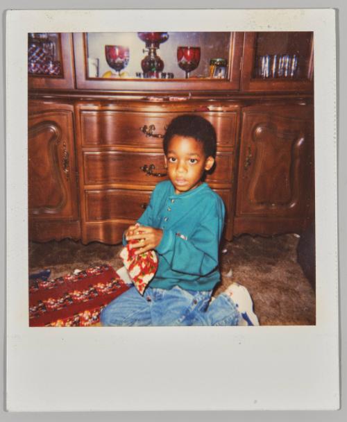 [Boy sitting on ground holding floral hankerchief]
