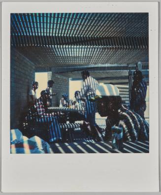 [People sitting at tables beneath roof with slates with sunlight causing patterned lines]
