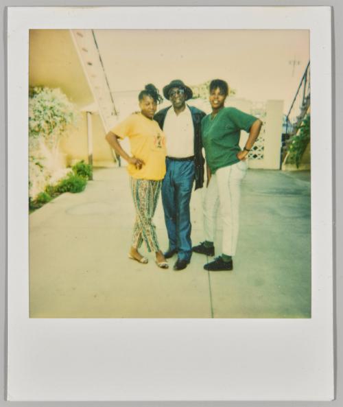 [Two women and man posing in front of white gate and staircase]
