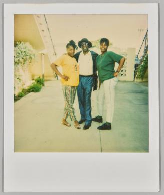 [Two women and man posing in front of white gate and staircase]
