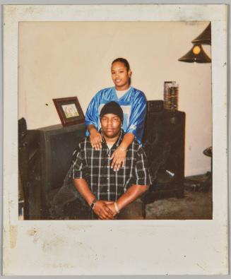 Monah [Woman in blue jersey embracing seated man]
