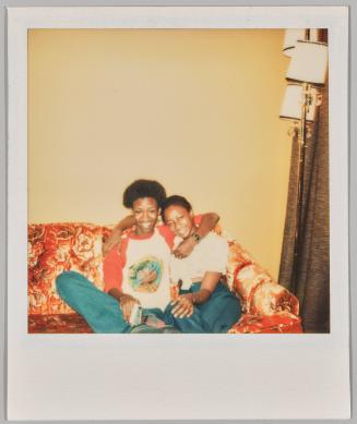 [Young man and woman embracing on orange floral couch]

