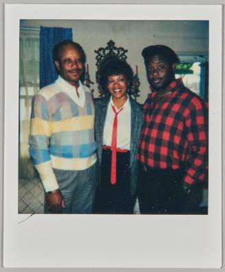 [Woman wearing red tie posing with men on either side of her]

