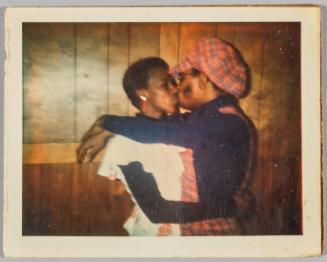 [Man in matching plaid overalls and hat kissing woman on lips]

