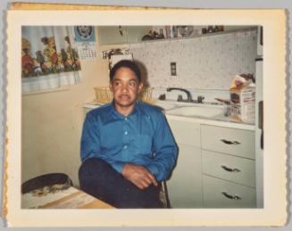 [Man sitting beside kitchen sink with carton of milk on counter]
