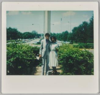[Adolescent boy and girl dressed formally standing in front of parking lot]
