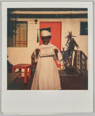 [Child in graduation gown holding kindergarten diploma]
