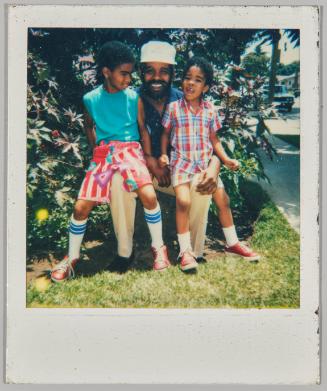 [Man wearing white hat sitting with two young boys on either knee]
