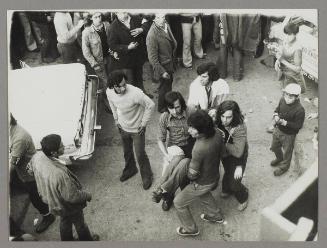 [A group of men carrying an injured woman to safety]
