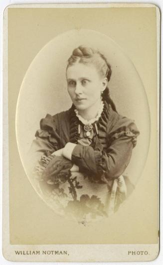 [Young woman sitting with arms folded over the back of a chair]