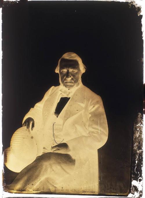 Portrait of a seated man, his legs crossed and holding a hat in his right hand