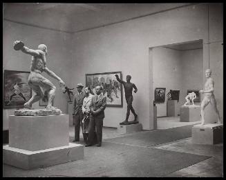 Three men (with Nazi insignias) inside a gallery - exhibiting sports themed paintings and sculptures.