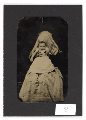 Portrait of baby in white dress (held by shrouded figure)