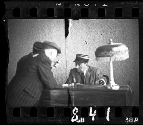 A Jewish policeman sitting at a desk, with another policeman and an unidentified man