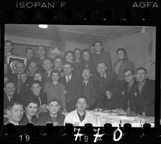 Large group of residents at a recpetion in the ghetto; man holding a framed award in the back