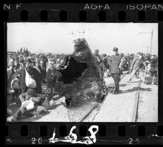 Jewish police and residents gathered in the street beside a railroad track, awaiting deportation
