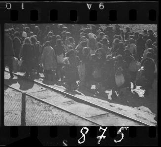 Large group of residents being deported from the ghetto, walking along a railroad track with their bundles on their backs