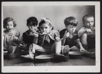 Five children sitting on floor and eating