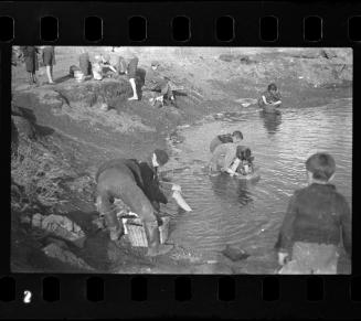 Children in a pond searching for items to salvage